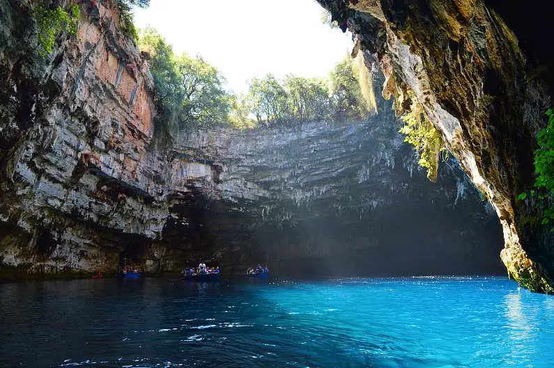 Melissani Lake with light shining through the opening in the cave roof with boats in the background