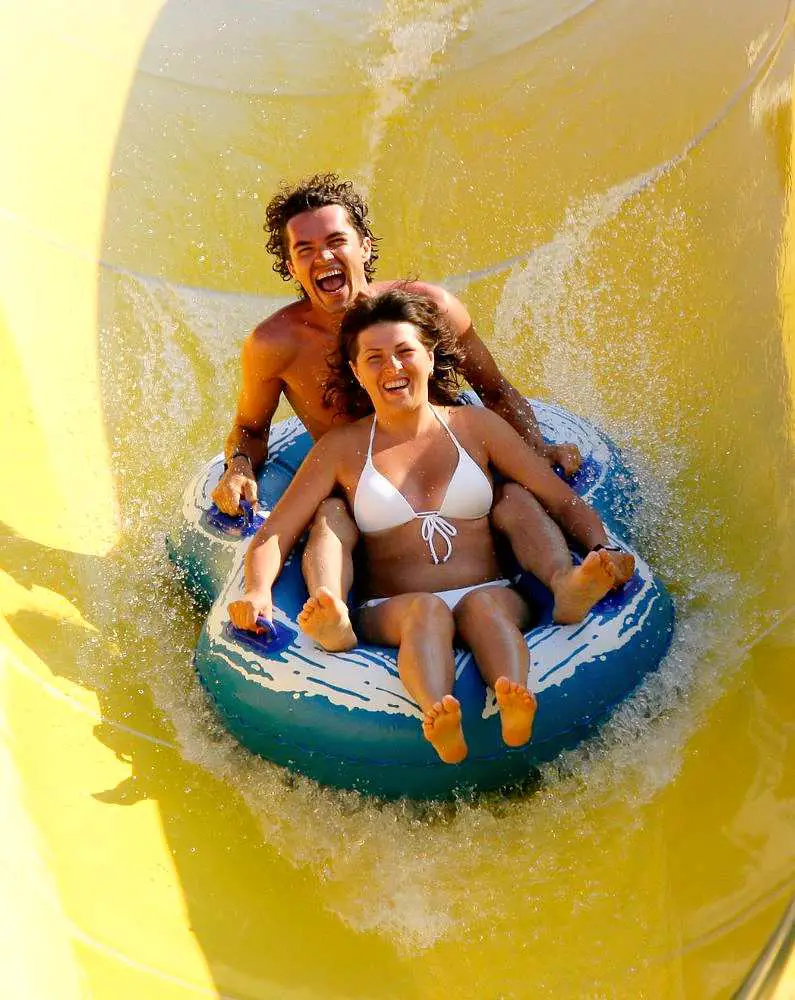 Man and woman in a rubber dingy laughing coming down a yellow waterslide