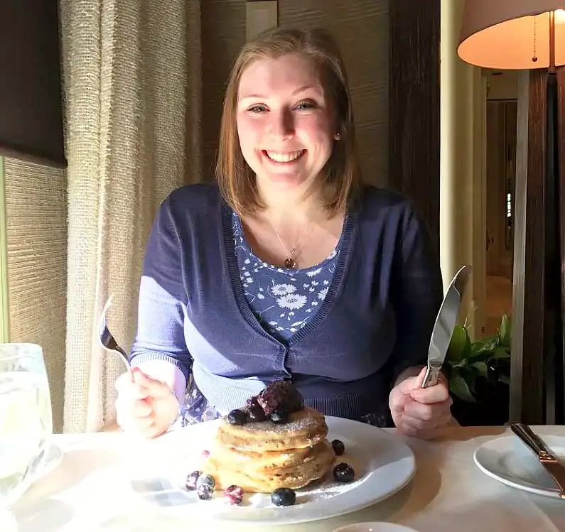 Mel wearing a blue dress and cardigan holding a knife and fork looking happy over blueberry pancakes at Tableau in the Wynn Hotel Las Vegas