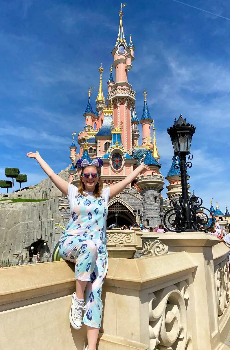 Mel wearing Minnie Mouse ears with her arms up by Sleeping Beauty's Castle in Disneyland Paris