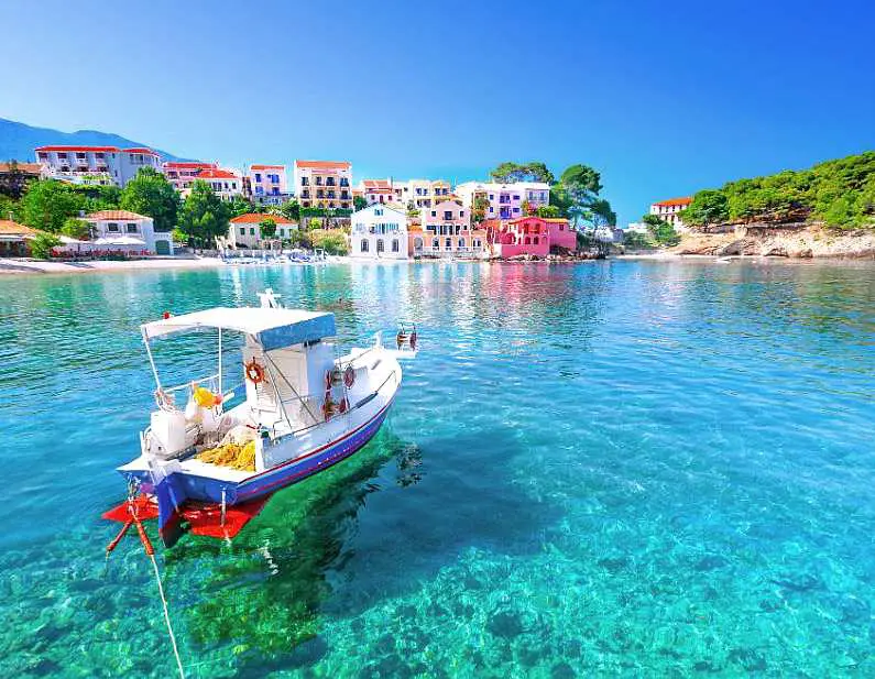 White and blue boat floating near Assos village in Kefalonia with colourful villas in the background