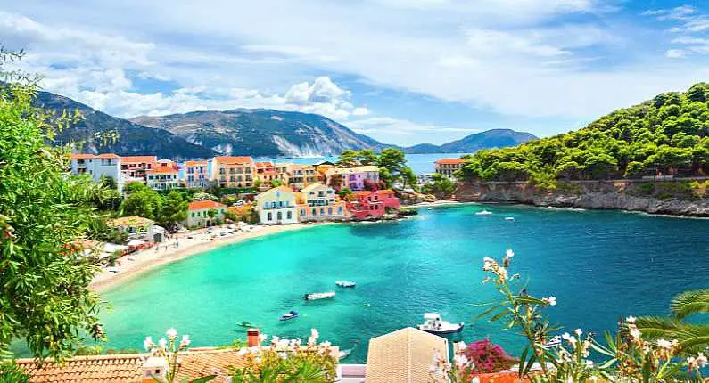 Pinterest image of Assos village in Kefalonia with colourful villas around a beach cove and blue water and mountains in the background 