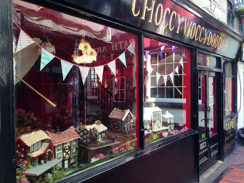 Outside the shop front of Choccywoccydoodah with black wood panels and a window filled with chocolate cake houses and bunting