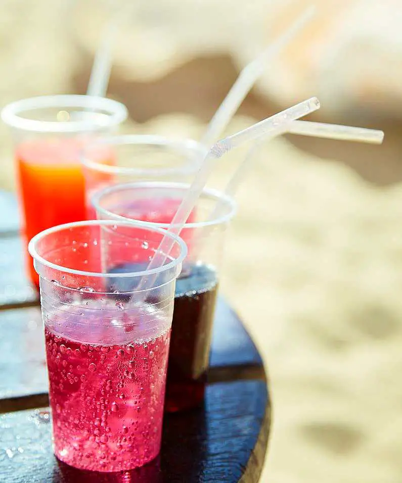 A row of different coloured cocktails in plastic cups with straws 