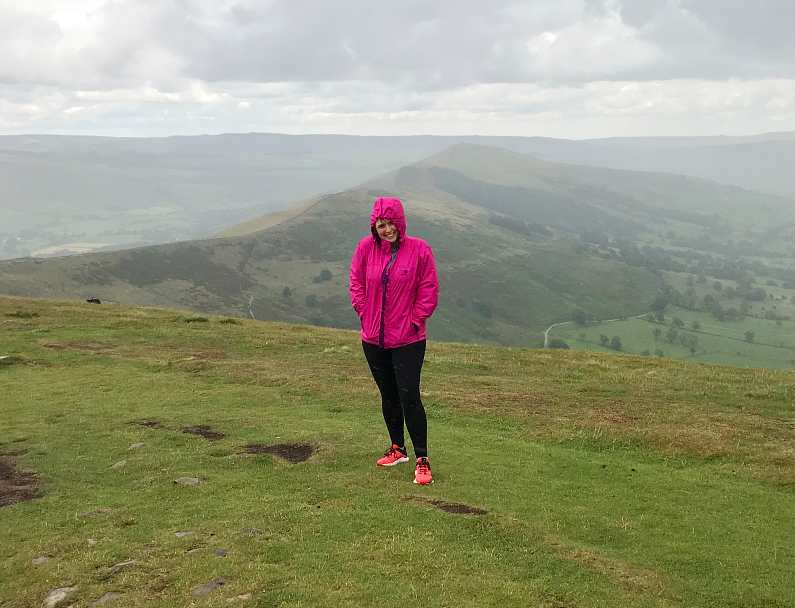 Mel at the top of Mam Tor during a rain storm wearing a pink waterproof jacket