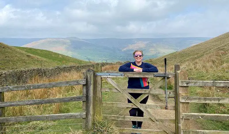 Mel leaning on a gate on the descent from the summit of Mam Tor with peaks in the background