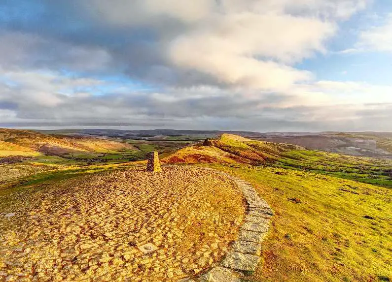 Summit stone at Mam Tor from afar with a stone path leading to it at golden hour