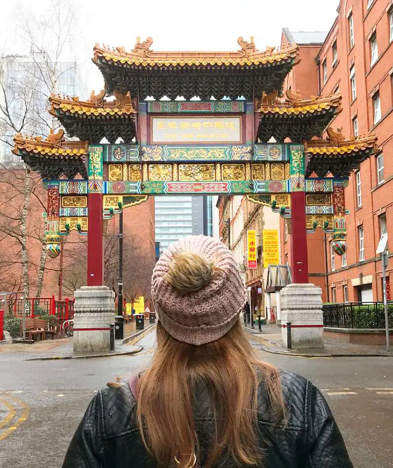 Mel stood in front of the ornate Chinatown sign in Manchester wearing a pink bobble hat