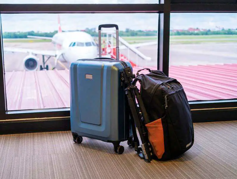 Suitcase and backpack on the floor at the airport in front of a window with a plane in the backgroun 
