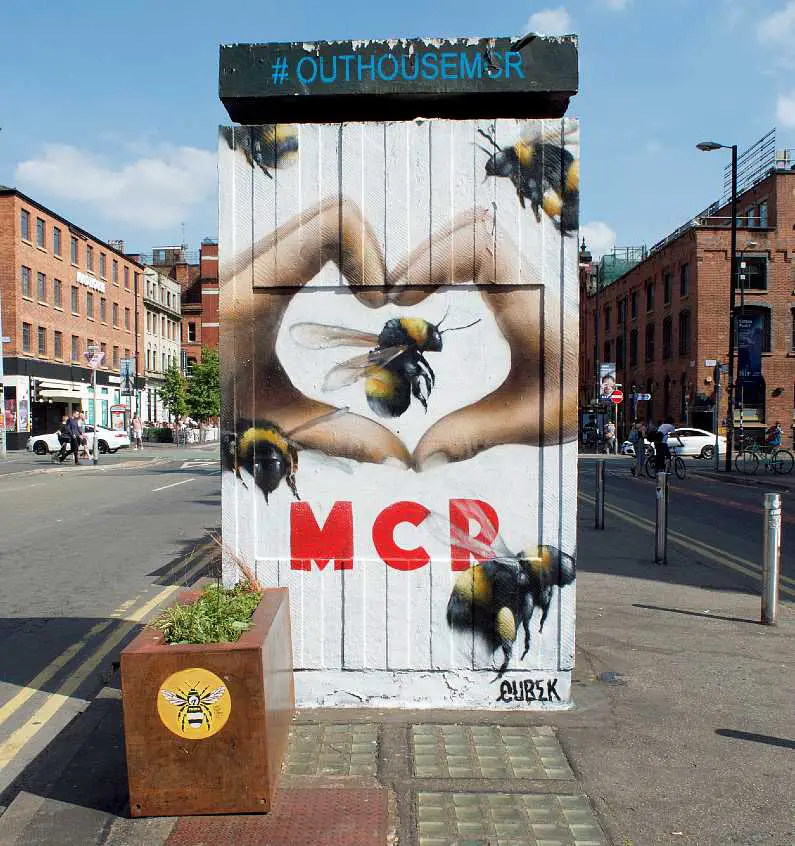 Street art of a pair of hands making a heart with "Mcr" underneath with bees flying all around