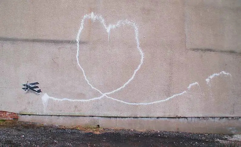 Photo of Banksy street art in Liverpool of a vintage plane flying leaving a love heart cloud trail behind it