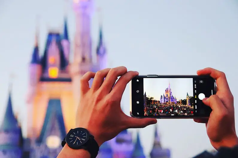 Person's hands holding up an iPhone to take a picture of Sleeping Beauty's Castle