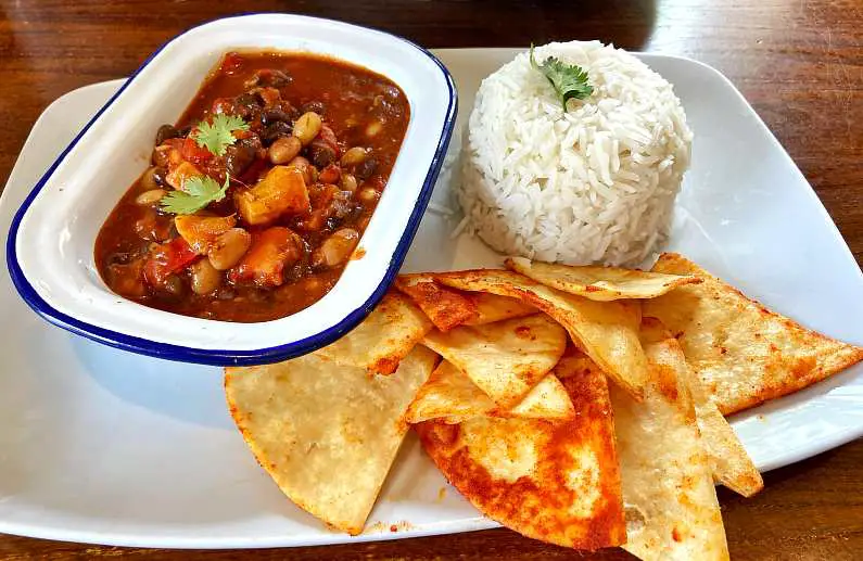 Dish of vegan five bean chilli with white rice and paprika tortilla chips