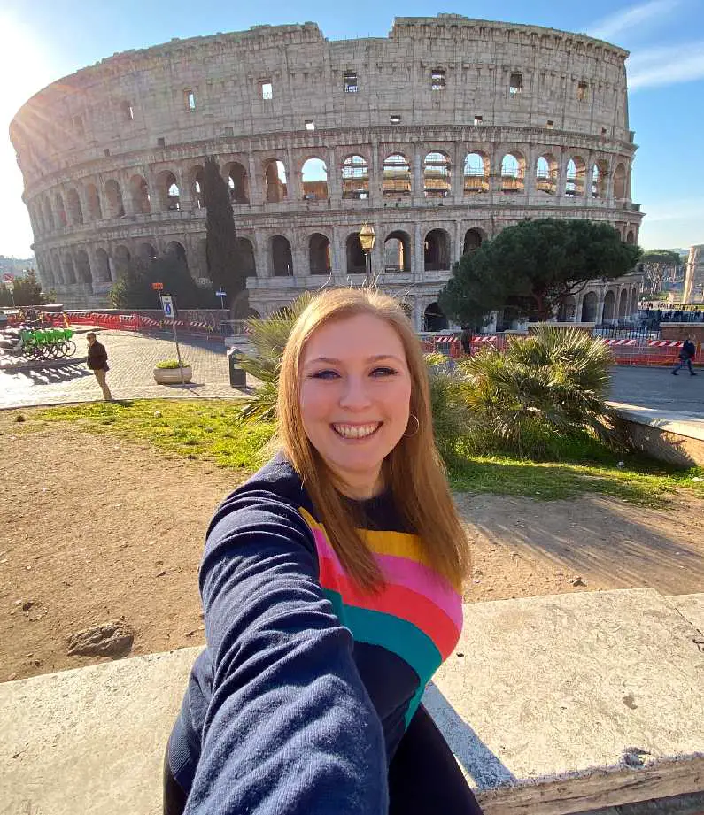 Mel taking a selfie in a rainbow jumper in front of the Colosseum in Rome
