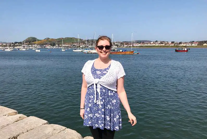 Mel standing by Conwy quayside with the marina in the background and boats sailing
