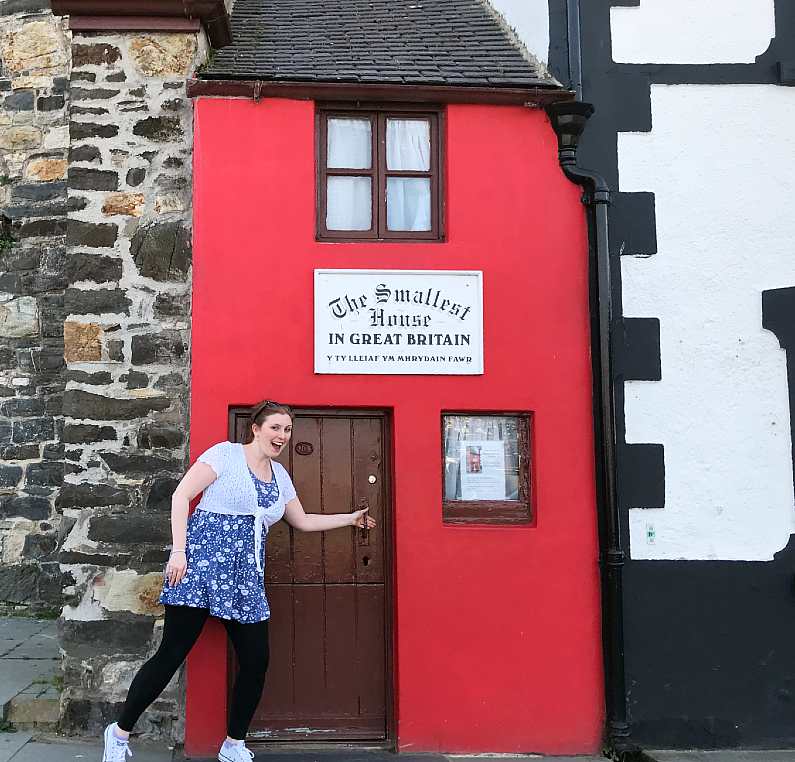 Mel stepping into the smallest house in Britain - a tiny bright red terrace house on the quayside of Conwy