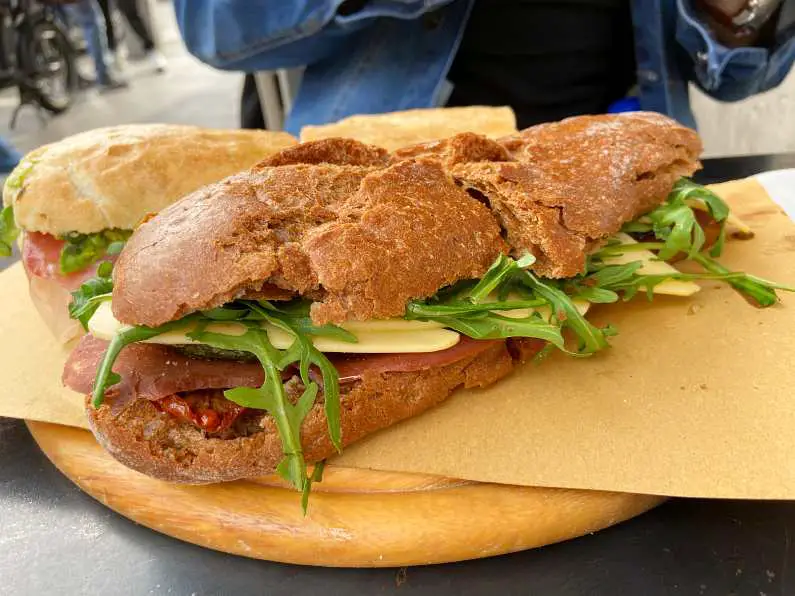Vegan deli sandwich with brown crusty bread, vegan cheese, vegan salami, sun dried tomatoes and rocket