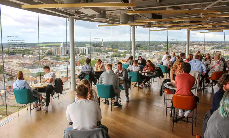 People sat at small tables in the Gravity Bar at the Guinness Storehouse with a skyline view of Dublin