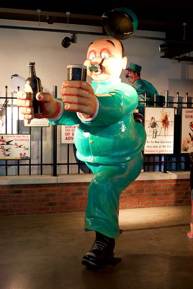 Statue of a portly cartoon man from an old Guinness advertising campaign wearing green and holding a pint of Guinness in one hand and holding a glass in the other