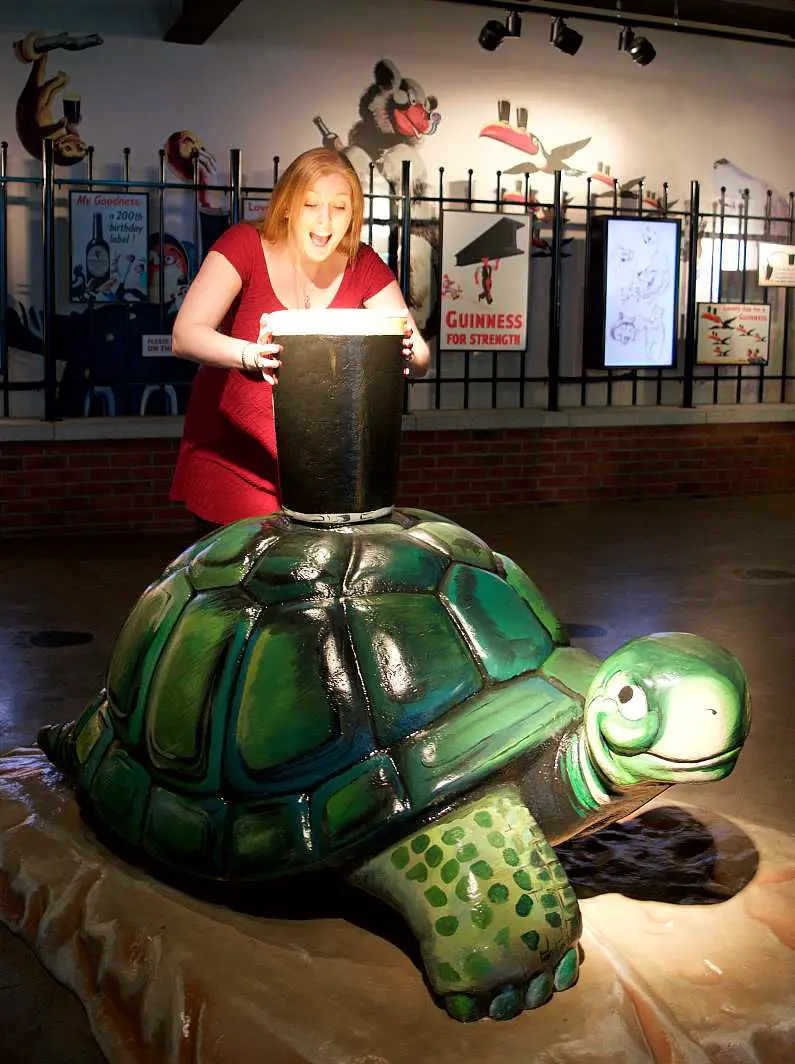 Turtle cartoon statue with a pint of Guinness on top of it with Mel pretending to drink from the giant pint glass