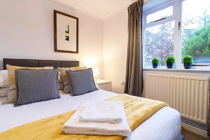 Double bed with yellow and white bedding and folded towels on it next to a bright window with three mini planters on the window sill