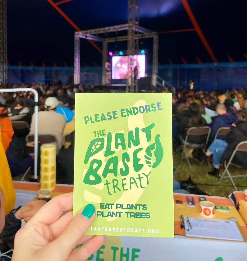 Mel's hand holding up a Plant Based Treaty flyer with the stage and audience in the background