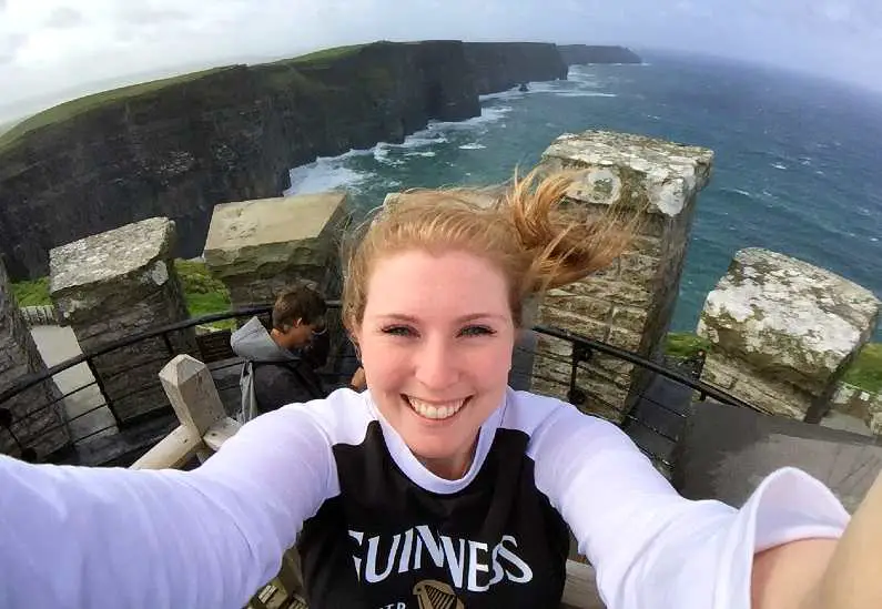 Mel taking a selfie at the top of a mini castle at the Cliffs of Moher in Ireland wearing a Guinness t-shirt