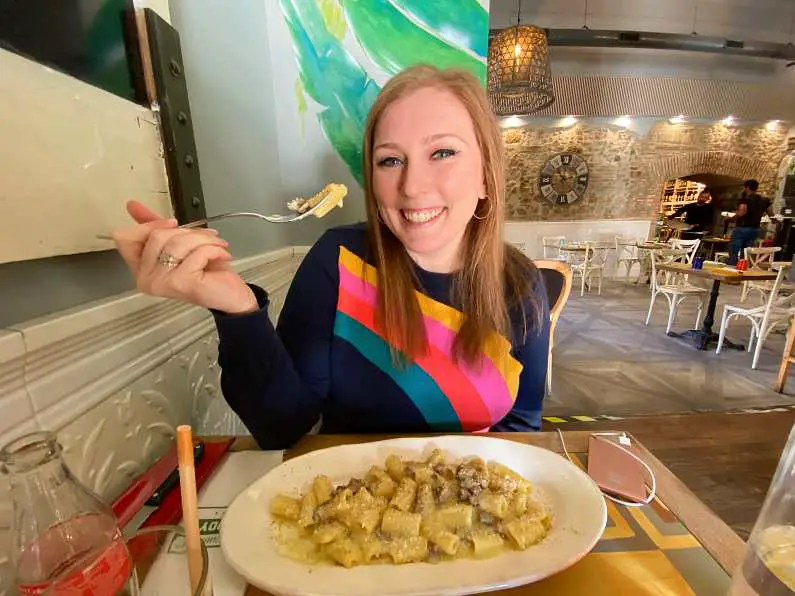 Mel holding a fork with pasta on it with a plate full of carbonara in front of her. She is wearing a rainbow jumper