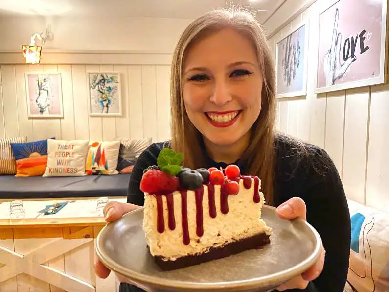 Mel holding a plate with a vegan cheesecake, chocolate biscuits base, soy yoghurt, raspberry sauce and fresh berries on top 