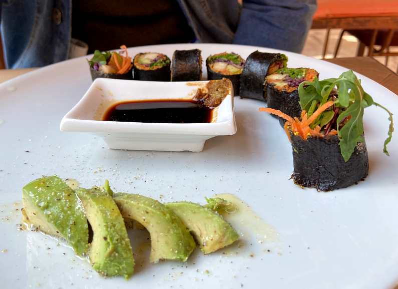 Plate of sushi rolls with sliced avocado and lentil sauce