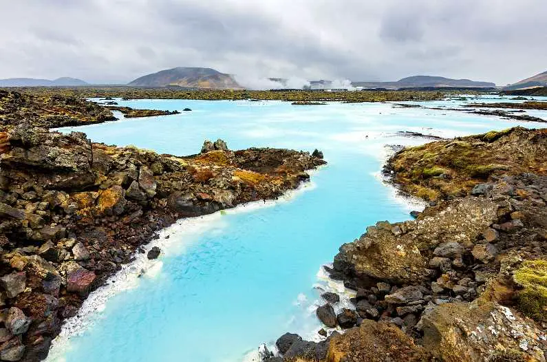 The bright blue water of the Blue Lagoon with jagged rocks on the edge of the pool