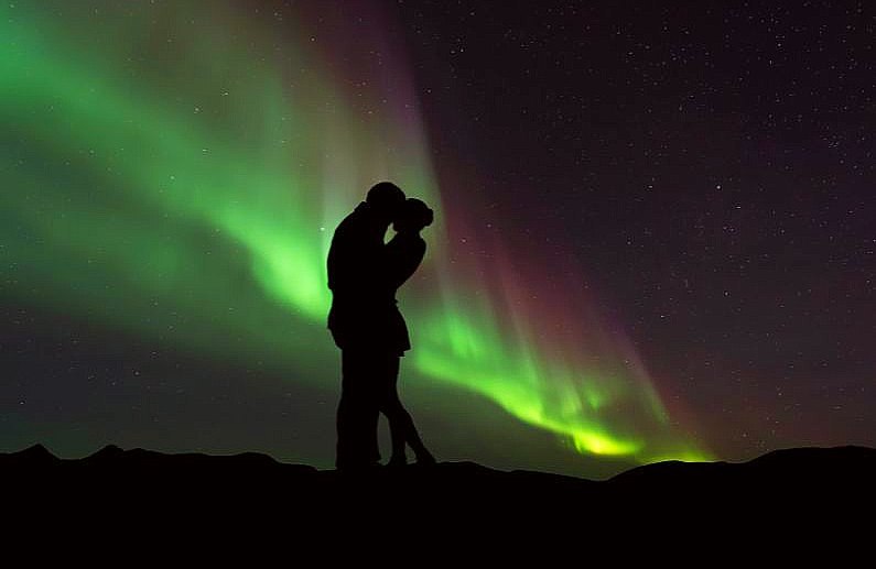 Dark outline of a couple holding reach other with the Northern Lights in the background