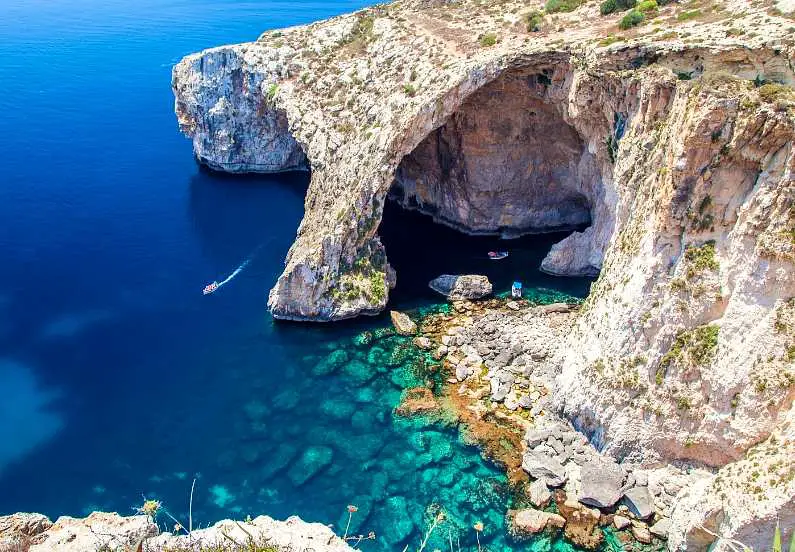Blue Grotto in Malta, a rocky arch with bright blue water around it with boats driving in and around it