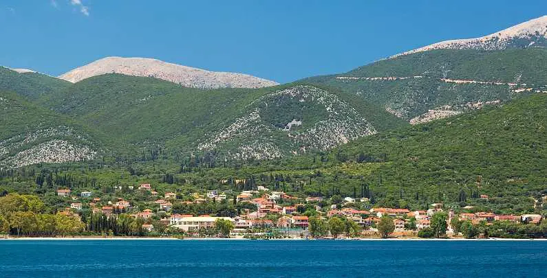 Skyline of Sami in Kefalonia with green mountains in the background and rows of orange topped houses on the edge of the sea in the foreground