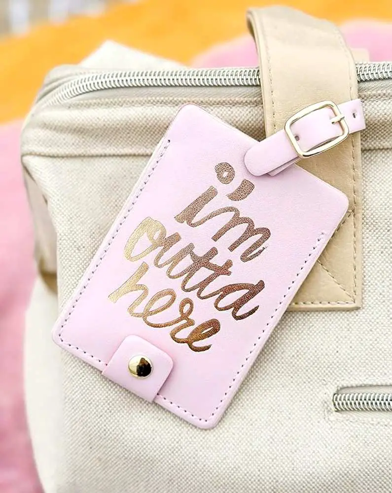 Pink luggage tag with the text: "I'm outta here" attached to a beige bag