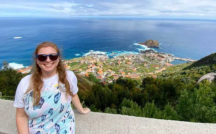 Mel wearing blue overalls and sunglasses smiling in front of the Madeira coast 