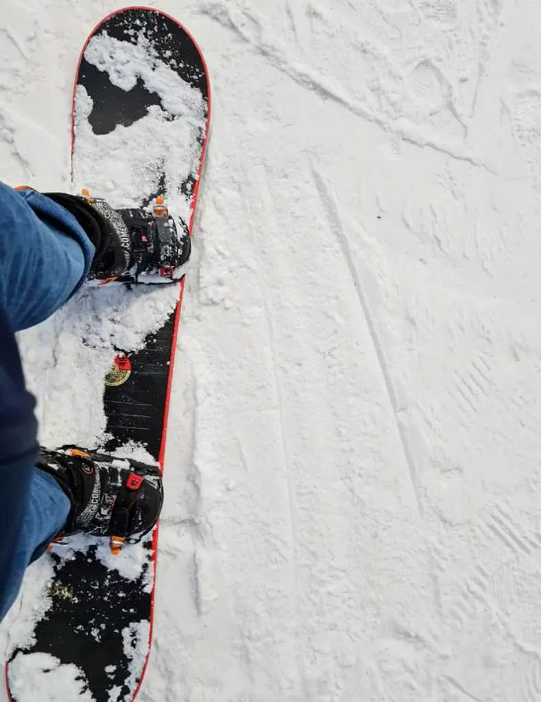 Point of view of legs and feet in a snowboard with snow all over the board
