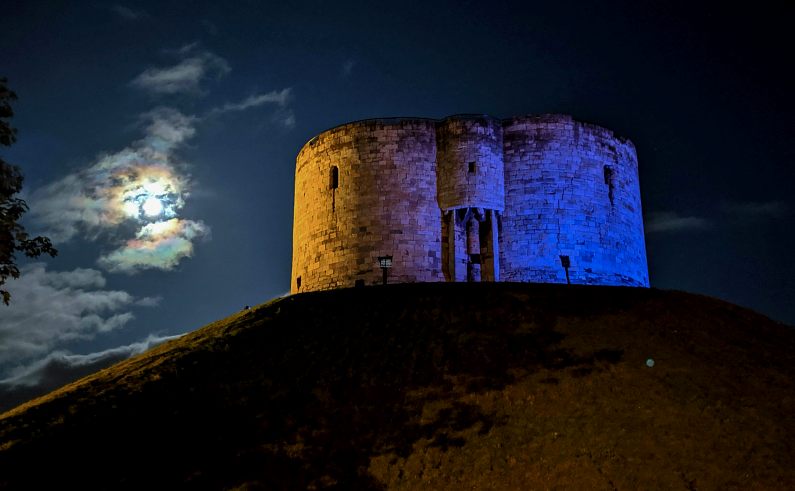 Clifford's Tower at night with the moon bright behind it