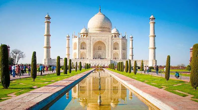 Image of the Taj Mahal, a white building with cone-like spheres on top in front on a still rectangular fountain